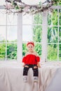 Little funny two years old girl child in stylish red clothes and jeans and sneakers on windowsill near window. With a smile On his Royalty Free Stock Photo