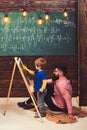 Little genius learning math. Teacher or father helping kid to solve equation on chalkboard. Bearded guy in pink shirt