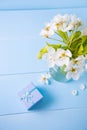 Little gift box and bouquet of tender white flowering branches in glass vase on blue wooden background Royalty Free Stock Photo