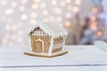 Little gingerbread house with glaze over defocused lights of Christmas decorated fir tree. Royalty Free Stock Photo