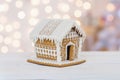 Little gingerbread house with glaze over defocused lights of Christmas decorated fir tree. Royalty Free Stock Photo