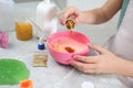 Little girl adding colored sparkles into slime toy at table, closeup of hands