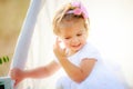 Little girl adjusts her hair of hut for games. Child with beautiful hairstyle in white dress.