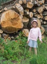 Little girl against stacked sawn wooden logs