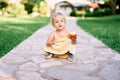 Little girl with apple in hand sits on a cobbled path in the park Royalty Free Stock Photo