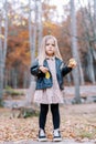 Little girl with an apple in one hand and a yellow leaf in the other is standing in an autumn park Royalty Free Stock Photo