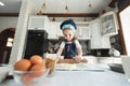 A little girl in an apron and a chef& x27;s hat is rolling out cookie dough, laughing Royalty Free Stock Photo