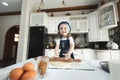 A little girl in an apron and a chef`s hat is rolling out cookie dough, laughing Royalty Free Stock Photo