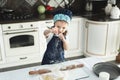 A little girl in an apron and a chef`s hat sprinkle the dough with flour in the kitchen