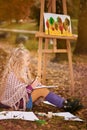 Little girl artist paints a picture on an easel in autumn in the park Royalty Free Stock Photo