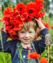 Little girl baby playing happy on the poppy field with a wreath, a bouquet of color A red poppies and white daisies, wearing a den Royalty Free Stock Photo