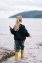 Little girl with a bag of garbage walks in shallow water near the beach. Back view Royalty Free Stock Photo