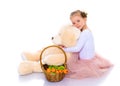 A little girl with a basket of flowers and a teddy bear is sitti Royalty Free Stock Photo