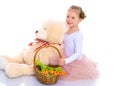 A little girl with a basket of flowers and a teddy bear is sitting on the floor. Royalty Free Stock Photo