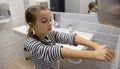 Little girl in the bathroom dries her hands with a hand dryer