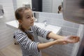 Little girl in the bathroom dries her hands with a hand dryer