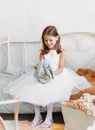 Little girl in a beautiful dress plays on the bed with a soft toy Royalty Free Stock Photo