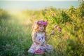 A little girl with beautiful long blond hair, dressed in a light dress and a wreath of real flowers on her head, in the Royalty Free Stock Photo