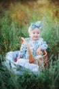 Little girl in a beautiful turquoise dress and a big bow on her head smiles and sits in a wicker basket in a green park, picnic Royalty Free Stock Photo