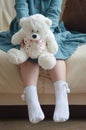 A little girl in a turquoise dress holds a white toy bear with a ribbon with hearts in her hands. a child`s toy. Royalty Free Stock Photo