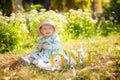 Little girl in a beautiful turquoise dress and a straw hat on her head, smiles and sits on a blanket in a green park Royalty Free Stock Photo