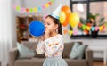 little girl in birthday party hat blowing balloon Royalty Free Stock Photo