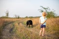 Little girl with black dog walking on the field back to camera in hot summer evening Royalty Free Stock Photo