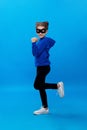Little girl in black mask, plays, cute robber smiling. Child masked bandit, over blue background. Vertical view.