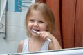 A little girl with blond hair brushing her teeth. The child is smiling at the reflection in the mirror. Royalty Free Stock Photo