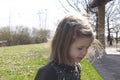 Little girl with blond hair and red hair clip standing on green grass in countryside, smiling. Childhood concept