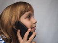 Little girl with blond hair talking on a smartphone, phone or tablet. Development of technologies and telecommunications, their Royalty Free Stock Photo