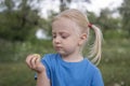 Little girl with blonde hair gathered in ponytails holds green apple in hand. Child spends time in nature Royalty Free Stock Photo