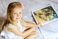 cute little girl with blonde hair reading book on the bed Royalty Free Stock Photo