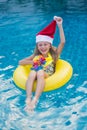 Little girl blonde in a Santa hat and swimming around in the pool, the concept of celebrating Christmas and new year in tropical Royalty Free Stock Photo