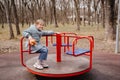 A little girl in a blue coat with a plush toy spins on carousel on playground.