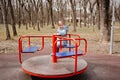 A little girl in a blue coat with a plush toy spins on carousel on playground.