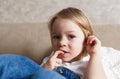 a little girl in a blue denim jumpsuit sits on the couch and bites her nails. Close-up.