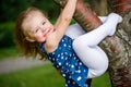 Little girl in a blue dress hanging on a tree branch Royalty Free Stock Photo