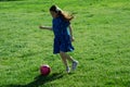 Little Girl in Blue Dress kicking soccer ball on Green Grass