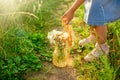 A little girl, in a blue dress, puts a knitted bag with a bouquet of daisies on a path in a field Royalty Free Stock Photo