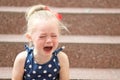 Little girl in a blue dress sits on the steps and cries Royalty Free Stock Photo