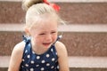 Little girl in a blue dress sits on the steps and cries Royalty Free Stock Photo