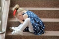 Little girl in a blue dress sits on the steps and cries Royalty Free Stock Photo