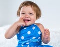 Little girl in a blue dress is sitting and laughing holding her finger in her mouth Royalty Free Stock Photo