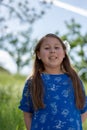 Little Girl in Blue Dress Smiling in Front of Field with Flowers