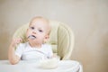 Little girl with blue eyes looks thoughtfully into the camera, licking a spoon with porridge Royalty Free Stock Photo