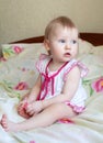 Little girl with blue eyes in a pink dress sitting on the bed Royalty Free Stock Photo