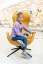 Little girl in a blue jumper sitting in a yellow chair