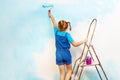 Little girl in blue paints the wall on a ladder