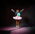 Little girl in blue t-shirt, denim jacket, poofy skirt, sneakers, sunglasses. Bouncing up against black background. Full length